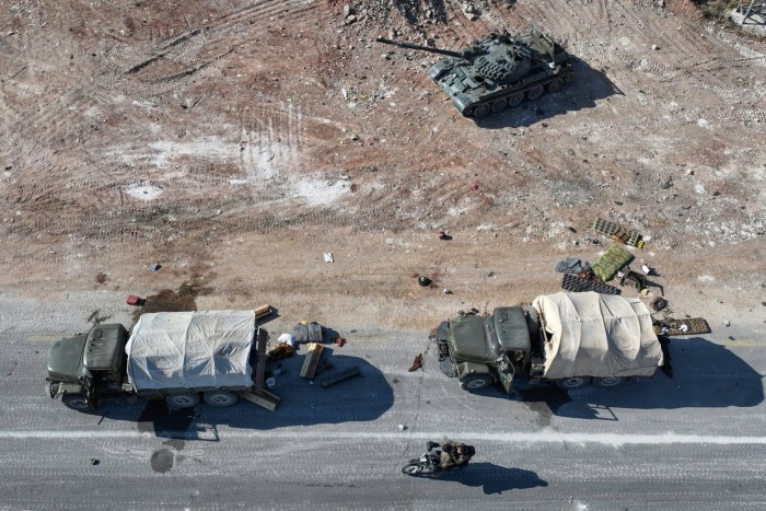 Антиправительственные боевики на мотоцикле проезжают брошенную военную технику и транспорт сирийской армии по шоссе, ведущему в Дамаск