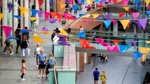 Люди идут по торговому центру Liverpool One. Территория украшена разноцветными треугольными флагами.