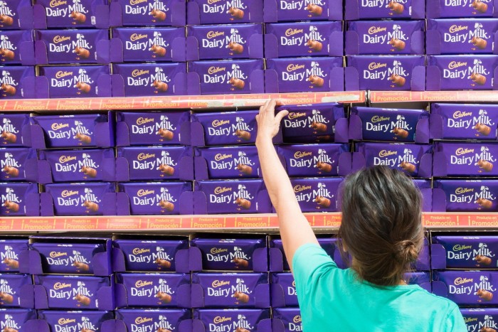 Женщина выбирает плитку молочного шоколада Cadbury на витрине супермаркета.