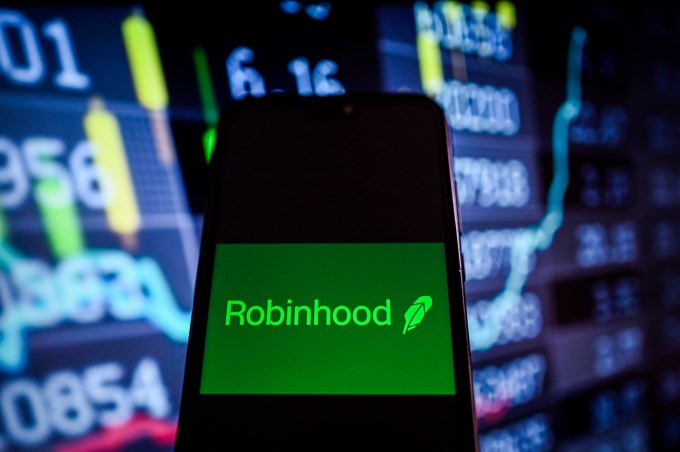 На этой фотоиллюстрации показан логотип Robinhood, отображаемый на смартфоне, на фоне которого отображаются проценты фондового рынка.