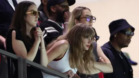 Reuters Taylor Swift, одетый в белый жилет, наклоняется к некоторым перилам в Super Dome в Новом Орлеане