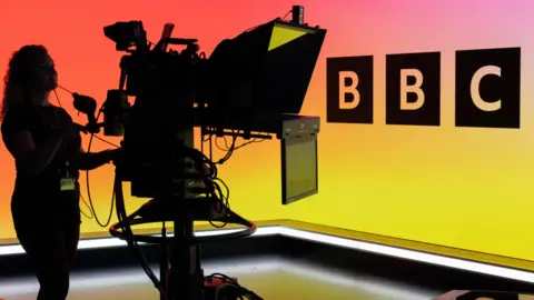 За кулисами BBC TV Studio (Plymouth), телевизионная камера и логотип BBC на светодиодной стене.