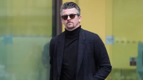 PA Media Joey Barton, в оттенках и длинное темно -синее пальто, выходя из здания суда.