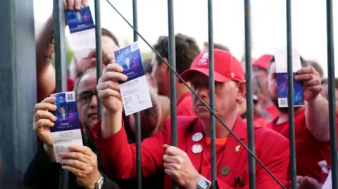 PA Media Liverpool Fans Clate в красных рубашках держите свои билеты на финальный матч Лиги чемпионов 2022 в Париже из -за железных ворот