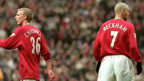 Getty Images Люк Чедвик, изображение в середине шага в рубашке Manchester United. Дэвид Бекхэм, справа от Чедвика, лицом к камере с камерой, а его рубашка «Красная Манчестер Юнайтед» номер 7 на полном дисплее.