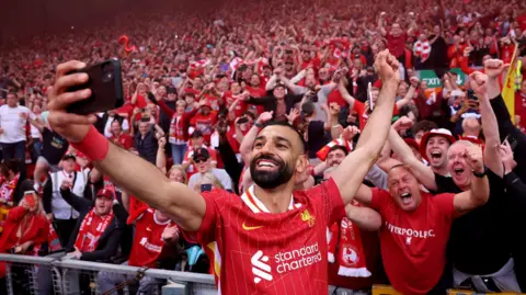 Reuters Mo Salah делает селфи на Anfield с фанатами, приветствующимися на стенде позади