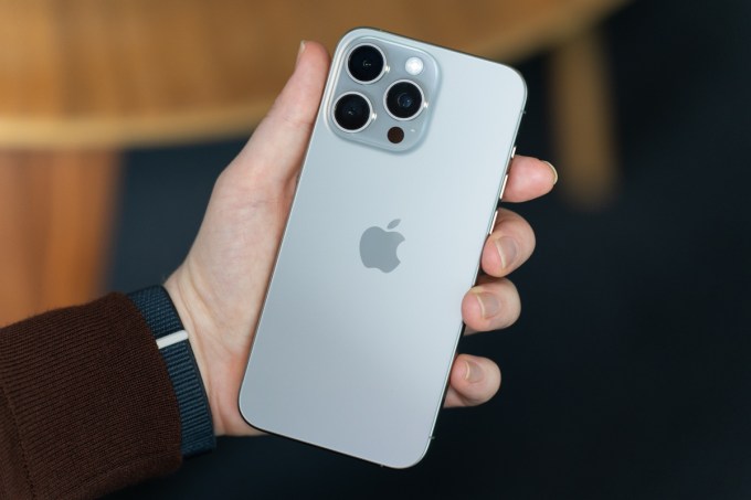iPhone 15 Pro Max в натуральном титане, который удерживается, показывая заднюю часть телефона