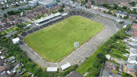 PA Media - вид с воздуха на Casement Park, пустой футбольный стадион, с жилищными застройками в окрестностях. 
